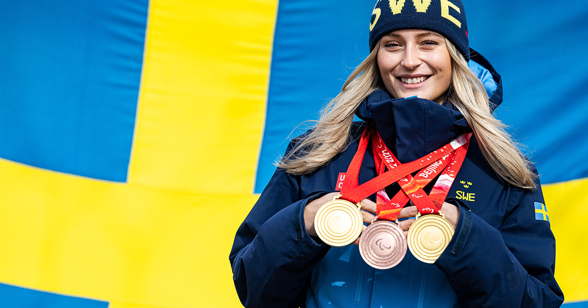 Ebba Årsjö visar upp sina medaljer från Paralympics framför en svensk flagga